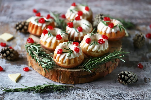 Рождественские кексы с розмарином, белой глазурью и красными ягодами. Элегантные праздничные торты. Рождественская композиция.
