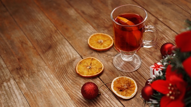 Christmas mulled wine in glass cup on a wooden table with dry oranges