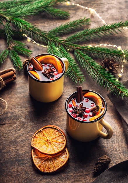 Christmas mulled wine with cranberries orange and spices in mugs on rustic plywood background