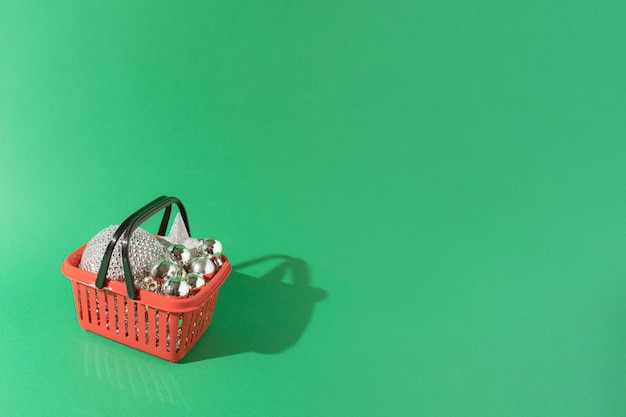 Christmas and New year 2022 concept. Basket full of shiny disco ball decoration and other silver christmas tree decorations on green background. Minimal copy space concept.