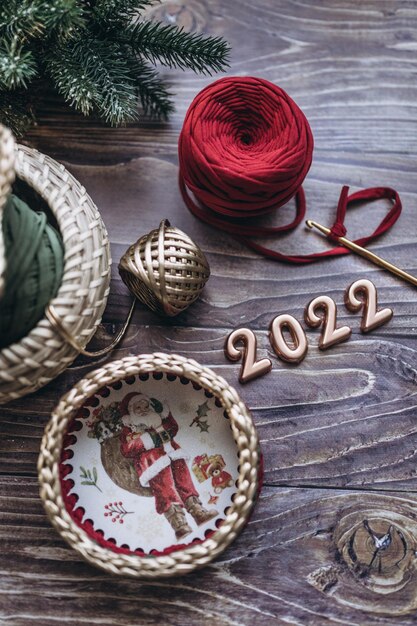 Christmas and New Year 2022 greeting card, balls of knitted yarn, crochet hook and knitted basket on a wooden table, top view