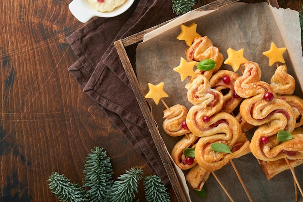 크리스마스 또는 새해 애피타이저 크리스마스 트리 모양 치즈와 햄을 곁들인 퍼프 페이스트리 빵 나무 보드에 있는 크리스마스 트리 모양의 그룹 크리스마스 또는 새해 저녁 식사를 위한 축제 아이디어