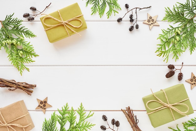크리스마스 또는 새해 준비. 흰색 나무 배경에 선물 상자, 침엽수 가지, 자연 장식으로 만들어진 프레임입니다. 평평한 평지, 평면도, 복사 공간.
