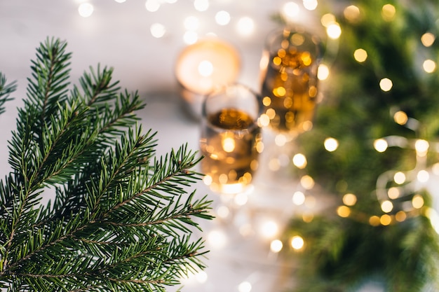 Christmas and New year background with fir branches, champagne glasses and glowing bokeh garland. Selective focus.