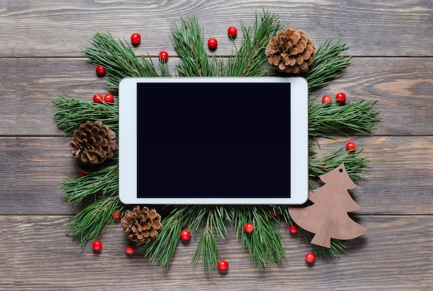 Christmas or new year background on a wooden background. Tablet with a blank screen for greetings. Flat lay, top view, copy space.