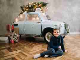 Photo christmas or new year card with a happy boy and a decorared retro blue car in the studio