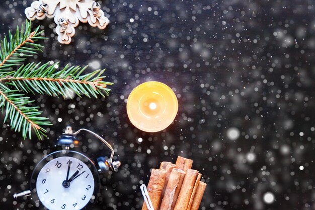 Christmas New Year Composition frame made of winter objects fir branch ornament candle clock on dark black background, snowflakes. Flat lay top view copy space. Christmas december time for celebration