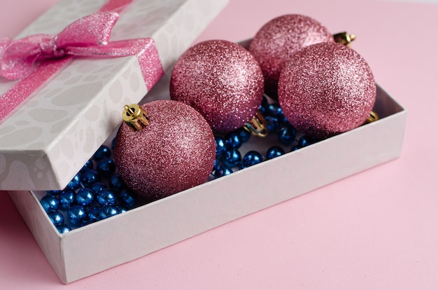 Christmas and New Year composition. Gift box with baubles on pastel pink . Flat lay copyspace.  .