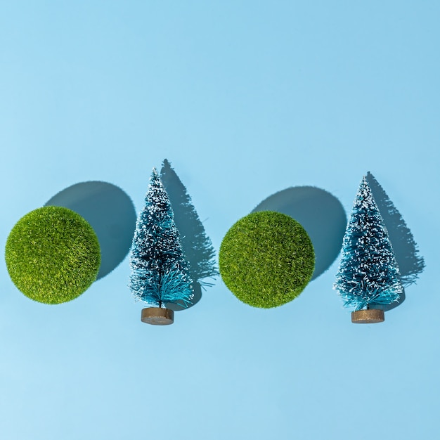 Christmas and new year conceptual background with small christmas trees and green balls on blue background. Trendy hard shadows, studio shot.