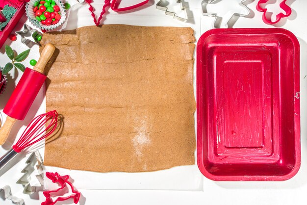 Christmas, New Year cooking background. Baking ingredients and utensils - gingerbread dough, cookie cutters, rolling pin. Making festive Christmas sweet cookies bright festive red white concept