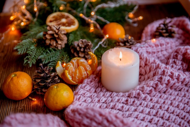 Christmas and new year decor. Christmas card. Tangerines, candle, lights, cones on a wooden background