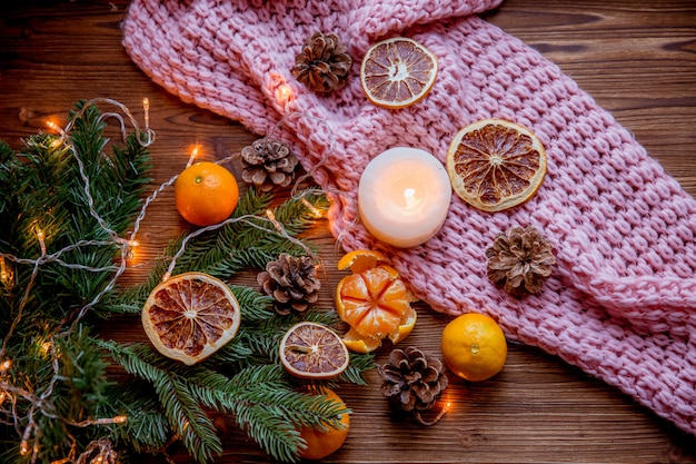 Christmas and new year decor. Christmas card. Tangerines, candle, lights, cones on a wooden background