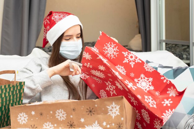 Photo christmas and new year during the coronavirus pandemic the girl in the mask collects gifts at home