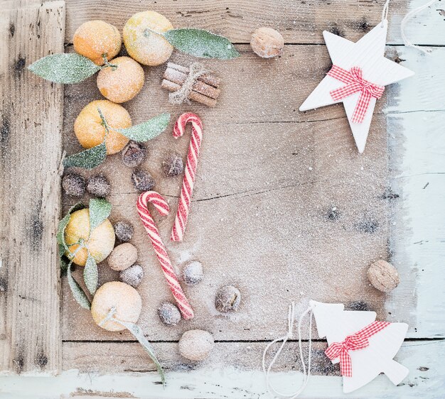 Christmas or New Year frame. Fresh mandarins, cinnamon sticks, walnuts, roasted chestnuts and candy canes covered with snow over rustic wooden  table