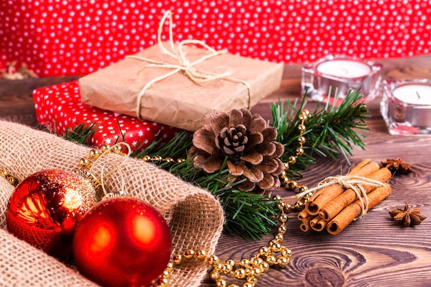 Christmas and New Year holiday background. Decor with fir branches, cones, Christmas decorations, beads, a gift wrapped in paper, cinnamon sticks, candles on a wooden table.