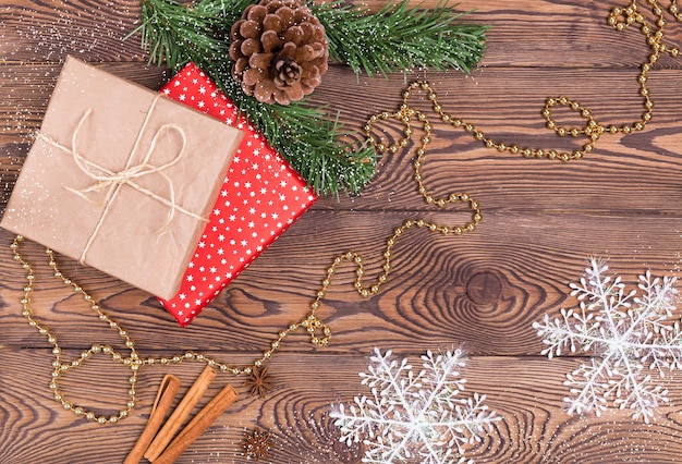 Christmas and New Year holiday background. Decor with gifts, fir branches, cones, Christmas decorations, beads, snowflakes, cinnamon sticks on a wooden table. Flat lay, empty space