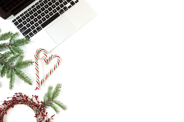 クリスマス年末年始の構成。ノートパソコン、クリスマスつまらないボール、モミの枝、白のキャンディースティックとホームオフィスデスクワークスペース