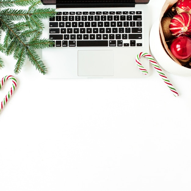 Christmas New Year holiday composition. Home office desk workspace with laptop, Christmas baubles balls, fir branches, candy sticks on white