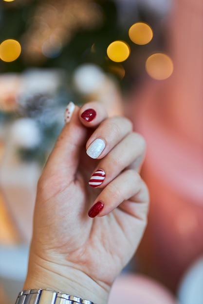 Christmas New Year manicure abstract nail design. Beautiful manicured woman's hand against the background of the christmas tree