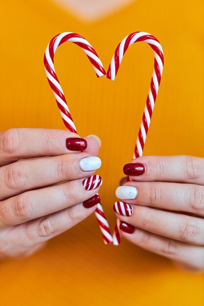 Christmas New Year manicure abstract nail design. Beautiful manicured woman's hand holding candy canes ornaments in the shape of a heart