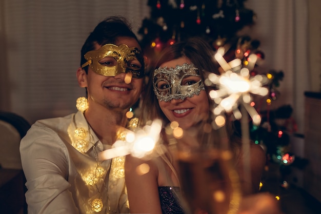 クリスマスと新年の仮面舞踏会パーティーのコンセプト照らされた木で線香花火を燃やすカップル