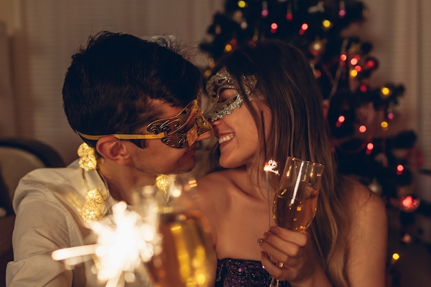 Christmas and New year masquerade party concept Couple burning sparklers by illuminated tree