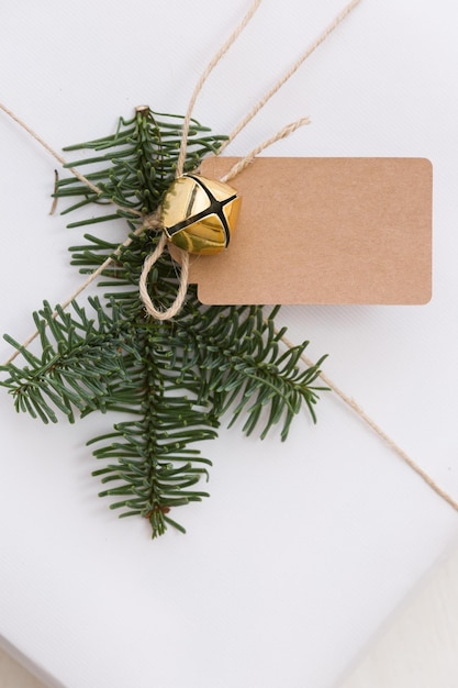 Christmas and New Year present with tag in white box with fir branches at white wooden table