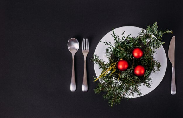 Christmas and New Year in a restaurant and cafe. In a plate are Christmas tree branches and Christmas balls. copyspace and flat lay on black.