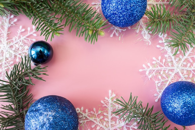 Christmas and New Year's layout on pink background, frame made of fir branches, snowflakes and toys, copy space.