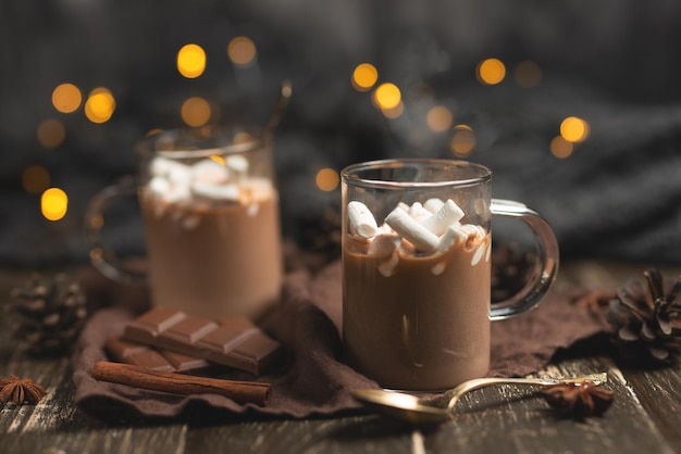 クリスマスまたは新年の冬のホット チョコレートとマシュマロを暗いマグカップに入れ、チョコレート シナモンとスパイスを添え、お祝いの光の花輪のセレクティブ フォーカス スクエア カルチャー