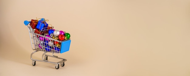 Фото Рождественские новогодние покупки макет с тележкой, подарками и украшениями на елочных шарах из ди ...