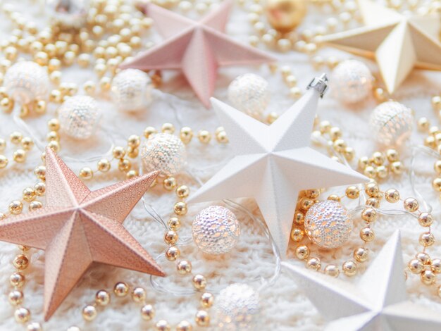 Christmas and New Year star decorations on white knitted . Metal light bulbs with delicate pattern, pale beige beads.