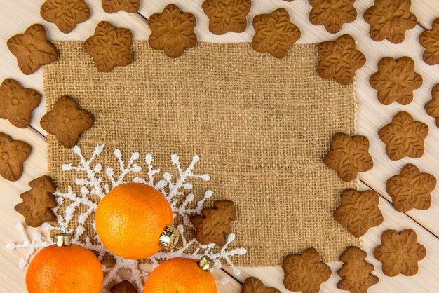 Christmas or New Year tangerines and gingerbread cookies with snowflakes framed on wooden background with brown sack background