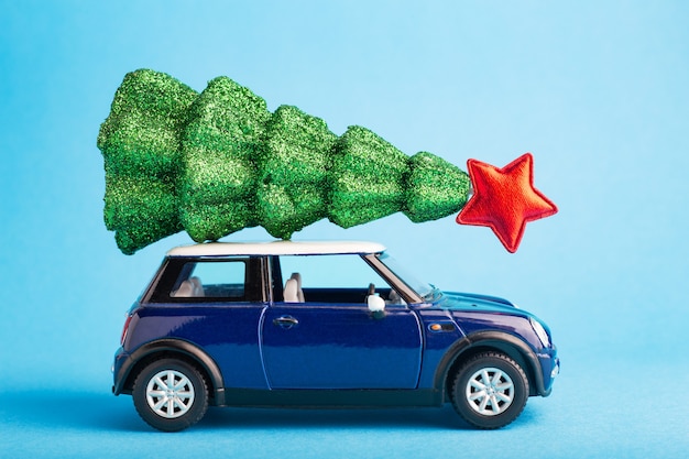 青い車のおもちゃの屋根の上に赤い星とクリスマスの新年の木。青い色の背景。車の上の創造的なミニチュアクリスマスツリー。