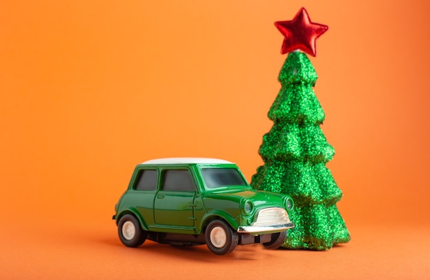 緑の車のおもちゃの近くに赤い星が付いたクリスマスの新年の木。オレンジ色の背景。創造的なミニチュアクリスマスツリーと車。ギフト配達のコンセプト。