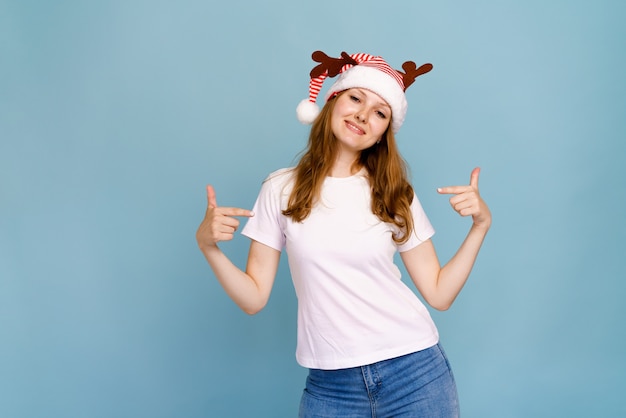 Christmas and new years concept happy santa girl with deer horns in white tshirt points her fingers ...