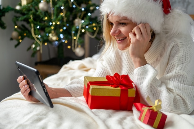 Christmas online shopping. Female buyer makes order on mobile phone. Woman buy presents, prepare to xmas, gift box in hand. Winter holidays sales