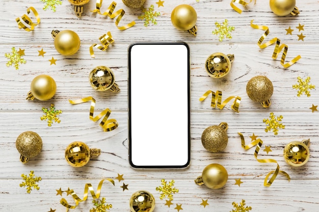 写真 クリスマスのオンラインショッピング - 空白のホワイトディスプレイのトップビュー スマートモバイル コピースペースとカラーの背景 クリスマスの装飾のボール 冬の休日販売の背景