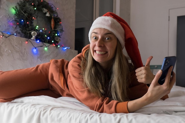 크리스마스 온라인 쇼핑: 스마트폰으로 빨간 산타 모자에 행복 한 여자. 온라인 상점을 통한 선물.
