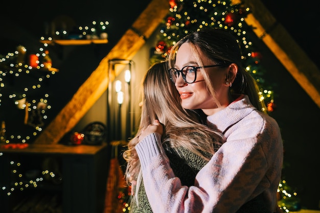 사진 크리스마스 또는 새해 축하, 두 젊은 행복한 여성이 크리스마스 트리 근처에서 서로를 껴안습니다.