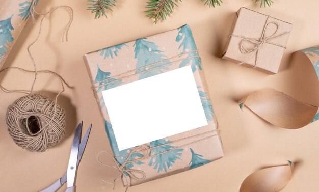 사진 크리스마스 또는 새해 diy 선물 상자는 베이지색 배경에 빈 공간이 있는 축제용 크래프트 종이로 싸여 있습니다. 크리스마스 선물 포장. 휴일 조롱. 공간을 복사합니다. 위에서 볼.