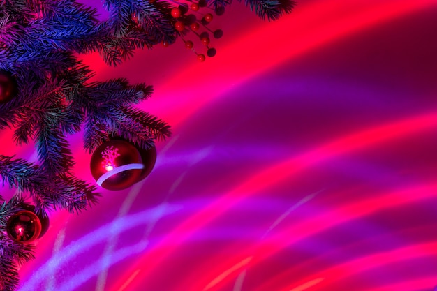 Christmas ornament and fir branches on a red festive background in neon light. Copy space.