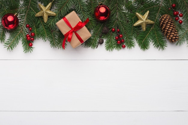 Christmas ornament. Green fir with red balls, golden stars and gift box on white wooden background, top view, copy space