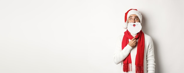 크리스마스 파티와 축하 컨셉의 재미있는 남자가 하얀 산타 수염 마스크를 들고 새해를 즐기고 있습니다.