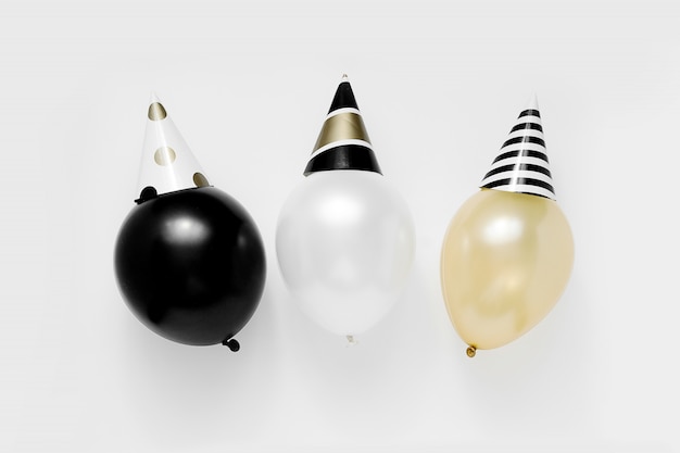 Christmas party concept. White, black and gold balloons in party hats on white background. Happy new year celebration