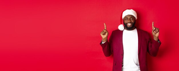 Christmas party and holidays concept handsome african american man in santa hat smiling pointing fin