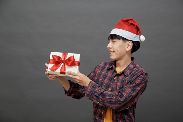 Рождественская вечеринка и концепция праздников. молодой азиатский мужчина, держащий подарочную коробку студии выстрел, изолированный на сером фоне