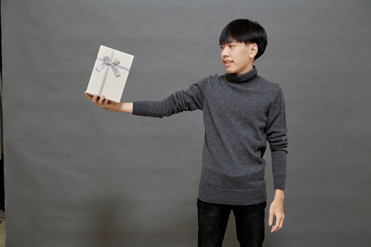 Photo クリスマスパーティーや休日のコンセプト。ギフトボックススタジオショットを保持している若いアジア人男性、灰色の背景で隔離