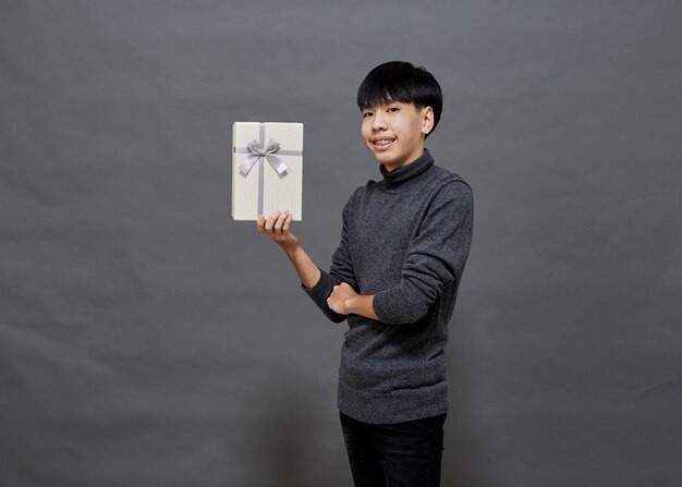 Photo christmas party and holidays concept. young asian man holding gift box studio shot, isolated on gray background