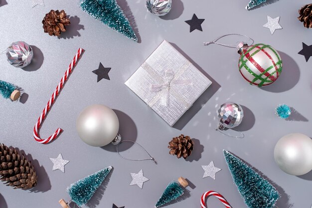 Рождественский узор с декоративной рамкой из подарков, леденцов, шариков и деревьев на сером фоне плоской планировки